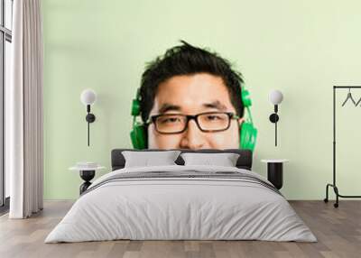 Headphones, music and portrait of Asian man in studio listen to audio, streaming podcast and radio. Mockup, subscription and face of happy person for entertainment, relax or chill on green background Wall mural