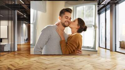 Home, couple and hug with kiss for love, affection and bonding together in marriage in house. Happy people, woman and man with cheek embrace for admiration, commitment and connection in relationship Wall mural