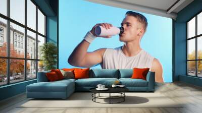 Man, drinking water and workout in studio for hydration, health and wellbeing on blue background. Guy, bottle and mineral liquid for electrolytes with fitness, exercise and training for wellness Wall mural