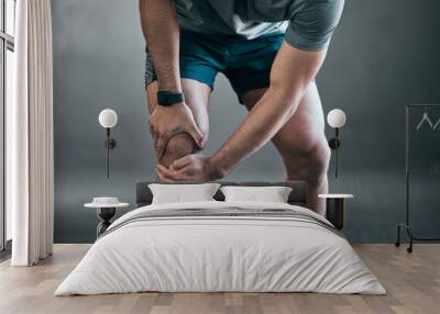 Man, hands and knee injury with pain in fitness from muscle tension or accident on a gray studio background. Closeup of male person with sore leg, ache or inflammation in strain, pressure or sprain Wall mural