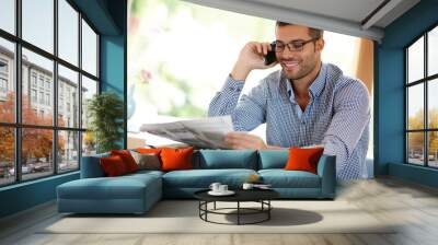 Man, home and phone call while reading a newspaper, morning routine and article for information. Male person, smile and app for conversation or networking, internet and story or weekend connection Wall mural