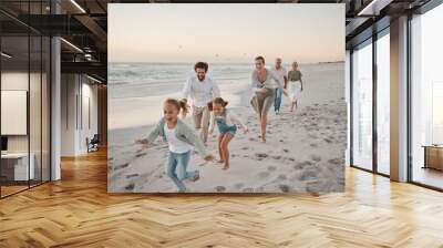 Parents, children and playful with running, beach and excited with grandparents on vacation in summer. Big family, kids and generations at sunset, care and bonding with games by ocean in Spain Wall mural