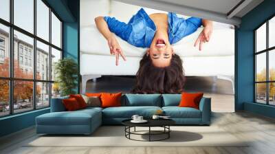 Peace sign, portrait and woman upside down on sofa in living room of home for weekend break. Emoji, hand gesture or smile and happy person relaxing in apartment with energy or excited for time off Wall mural