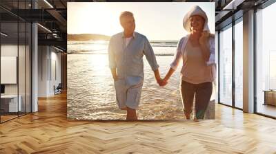 Senior, happy couple and holding hands with relax on beach sunset for support, love or bonding in nature. Man, woman or lovers walking with smile on outdoor summer holiday by water or ocean coast Wall mural