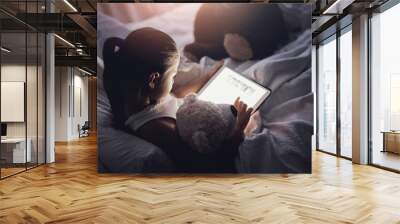 Tablet, reading and kid at night with ebook, story and youth game with cartoon and language app. Tech, teddy bear and young girl with scroll, relax and evening screen time at home in bed online Wall mural