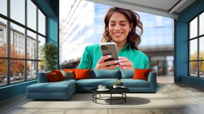 Young woman taking a city moment to browse her smartphone Wall mural