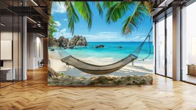 a hammock hanging between two palm trees on a tropical beach with clear blue water and a sandy shore with a rock formation in the background  Wall mural