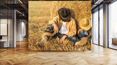 Father and son resting in the field wear hats, shirts and jeans. Son like as father concept Wall mural