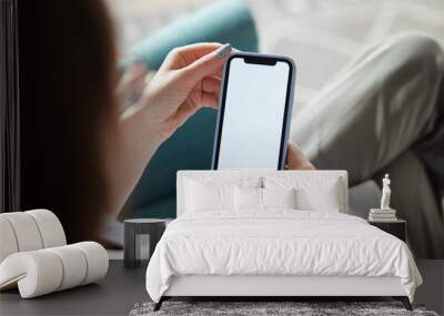 Mock up white screen blank mobile phone in woman hands holding sitting on armchair at home Back view Wall mural