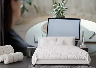 Mockup white screen laptop and mobile phone woman using computer sitting at table at home, back view Wall mural