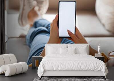 Young woman hold mobile phone in hands, lying on the sofa Wall mural