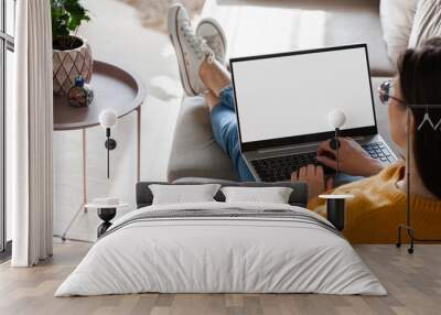 Young woman using laptop screen blank, mockup lying on sofa at home Wall mural