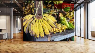 A close up view of a bunch of yellow bananas hanging from a market stall, displaying their fresh and ripe appearance. Fresh Bunch of Yellow Bananas at a Market Stall Wall mural