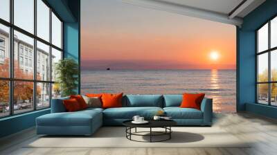 Ship at the sea in bright orange sunset / sunrise with sun in the background Wall mural