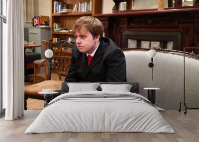 A young man looking glum in a suit sat on a sofa Wall mural