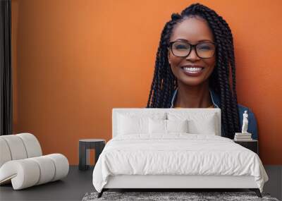 Cheerful Black Woman in Her Late Thirties with Long Braids and Glasses, Smiling Against an Orange Wall. Casual Outdoor Outfit Featuring a Denim Jacket Over a Yellow Sweater, Wall mural