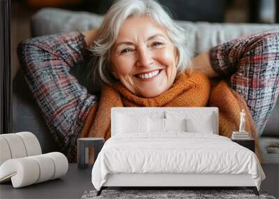 Cinematic medium shot of an older woman sitting on the couch with her hands behind her head, smiling joyfully as she relaxes at home. Wall mural