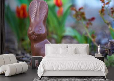 Close up of choco rabbit as an easter, sweets and confectionery concept - chocolate bunny or Easter bunny in the garden bed with blurred colorful tulips in the background, easter bunny Wall mural