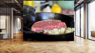 New York strip steak with potatoes frying in a cast iron pan on a natural gas stove top. Wall mural