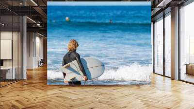 Person standing at the shore of the sea with splashing waves with a surfing board Wall mural