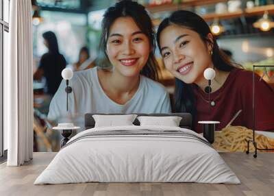 Two Young Asian Women's Joyful Dining Experience, Smiling Towards Camera in Restaurant, Noodles on Table, Chic Wardrobe, Natural Illumination Wall mural