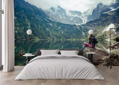 A young girl sitting on a stone by a mountain lake admires the views. Morskie Oko lake, Poland. Wall mural