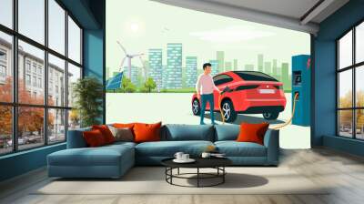 Modern electric suv car charging at the charger station with a young man holding the cable. Wind turbines and solar panels with urban landscape in background. Flat vector illustration concept.  Wall mural