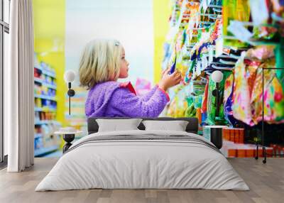 Adorable child blond girl select sweets on shelves in supermarket  Wall mural