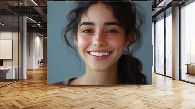 A cheerful young woman with curly brown hair and warm skin tone smiles brightly, radiating joy and positivity against a soft gray background. Wall mural