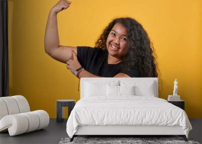 Attractive afro-american with overweight woman showing muscules, pointing finger on it, smiling over isolated orange background wearing fashion black shirt. People lifestyle concepte. Wall mural