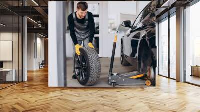 Car mechanic changing wheels in car Wall mural