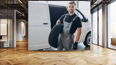 Car mechanic holding new tires by the white van Wall mural