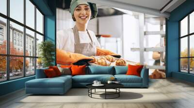 Female baker at the kitchen holding freshly baked croiisants Wall mural