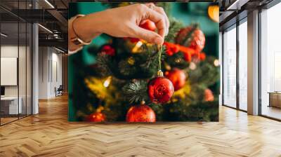 Female hands close up, decorating christmas tree with red toys Wall mural