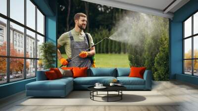 Garden worker watering grass and bushes in the yard with sprinkler Wall mural