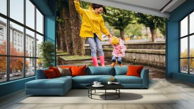 Mother with daughter having fun jumping in puddles Wall mural