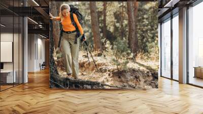 Woman hiking with walking sticks in forest stopped by the tree Wall mural