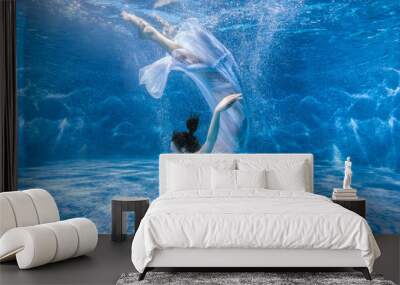 Woman in a white dress dives under the water in the pool. Wall mural