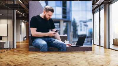 Young business man working on laptop and drinking coffee by the skyscraper Wall mural