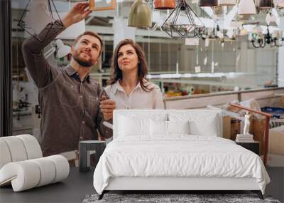 Young couple choosing chandelier in building center Wall mural