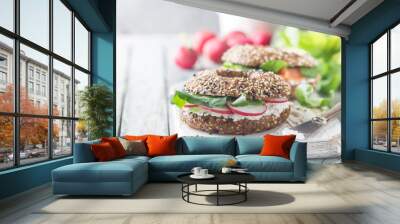 Bagels with cream cheese avocado, fish, arugula and radish on old wooden table. Healthy breakfast food. Wall mural