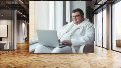 Overweight businessman in white clothes working with a laptop at home near the window Wall mural