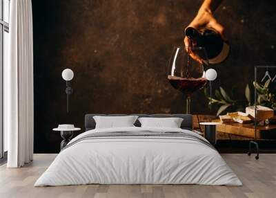 Pouring red wine into the glass against rustic dark wooden background Wall mural