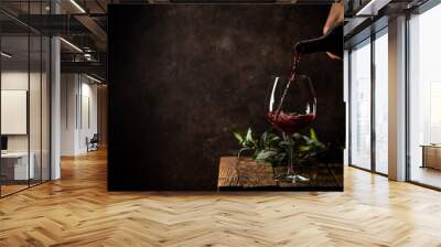 Pouring red wine into the glass against rustic dark wooden background Wall mural