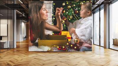 Cute baby and mum decorating a Christmas tree. Red balls. Wall mural