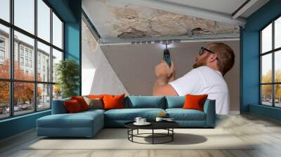 Construction worker assemble a suspended ceiling with drywall an. D fixing the drywall to the ceiling metal frame with screwdriver Wall mural