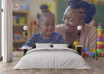 Teacher and toddler playing with maths puzzle game sitting on the table at kindergarten. Wall mural