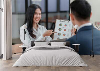 A woman is pointing at a chart while a man looks on. The woman is smiling and the man is wearing a suit. The chart appears to be a presentation or a report, and the two people seem to be discussing it Wall mural