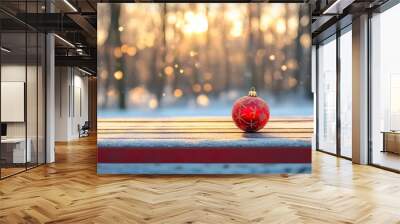 A bright red ornament with golden patterns sits on a snowy table as sunlight filters through trees, creating a peaceful winter atmosphere Wall mural