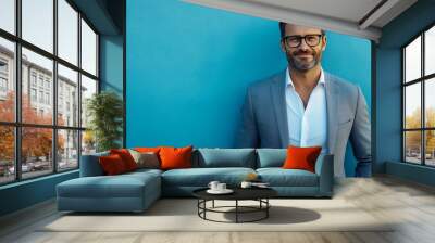 A confident man with glasses and a beard poses against a vibrant blue background, exuding professionalism and charm Wall mural